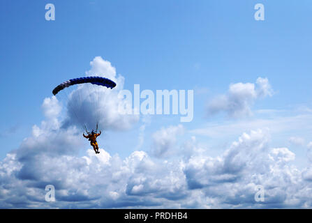 Skydiver under a dark blue little canopy of a parachute on the background a blue sky and clouds, close-up. Silhouette of the skydiver with parachute a Stock Photo