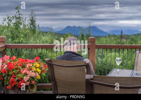 A senior man set on the deck of resort hotel lodge with glass of wine Stock Photo