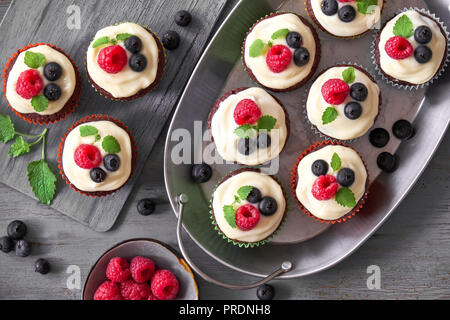 Chocolate muffins or cupcakes with whipped cream and berries, flat lay on gray rustic wooden background Stock Photo