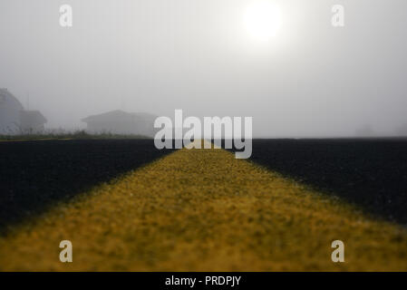 Marking on Empty Airport runway with buildings in a Fog. Empty runway at airport during a foggy morning. Sunrize over runway in a fog. Runway with yel Stock Photo