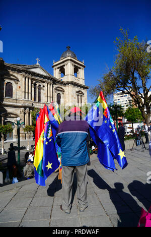 La Paz, Bolivia, 1st October 2018. A flag seller stands in front of the cathedral before the reading of the ruling for the case 'Obligation to Negotiate Access to the Pacific Ocean (Bolivia v. Chile)' at the International Court of Justice in The Hague. Bolivia presented the case to the ICJ in 2013; Bolivia lost its coastal Litoral province to Chile during the War of the Pacific (1879-1884) and previous negotiations have made no progress from Bolivia's viewpoint. Credit: James Brunker/Alamy Live News Stock Photo