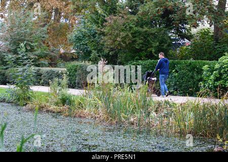 Hastings, East Sussex, UK. 2nd Oct, 2018. UK Weather: Autumnal weather and a slight breeze in the air with heavy rain expected later on. A man walks along a path with a pushchair in the Alexandra park in Hastings just the rain starts. © Paul Lawrenson 2018, Photo Credit: Paul Lawrenson / Alamy Live News Stock Photo