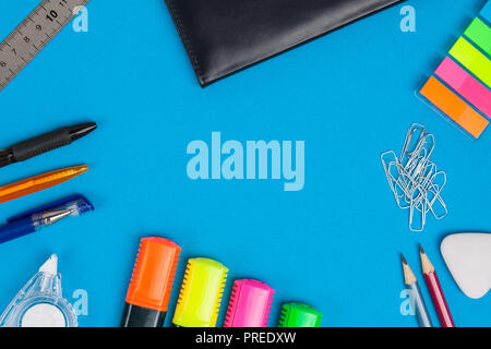 Notepad, pen, pencil, ruler, paperclips, eraser, markers and correction tape lie on blue background. Flat lay. Stock Photo