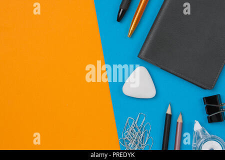 Pen, pencil, paperclip, eraser, correction tape and clip lie on blue background. Orange background with copyspace. Flat lay. Stock Photo