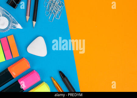 Two pens, two pencils, many paperclips, one eraser, three markers, one correction tape and one clip lie on blue background. Orange background with cop