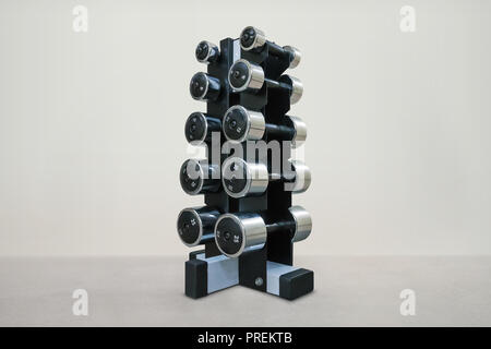 black metal stand with a chrome dumbbell on white background. Dumbbells of different weight category. Dumbbells with different weights Stock Photo