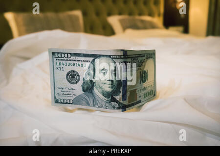 a good tip, some hundred dollars on the table on a blurred bed background. Tips at the bed for the housekeeper in hotel. Stock Photo