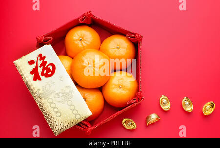 Group of orange tangerine in Chinese pattern tray and envelope packet ang pow with gold ingots on red table top. Chinese new year concep.Chinese Langu Stock Photo