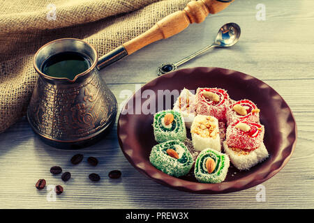 Turkish delight on clay plate with copper cezve with coffee beans on wooden board with piece of sackcloth Stock Photo