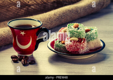 Cup of coffee with coffee beans and Turkish delight lying on saucer on wooden board with piece of sackcloth Stock Photo