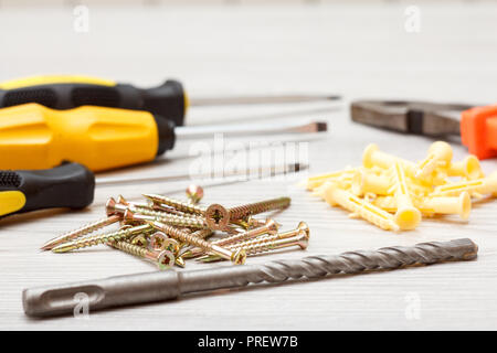 Screwdrivers, drill, pliers and screws with plastic dowels on white wooden background. Shallow depth of field Stock Photo