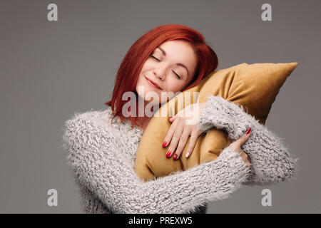 Studio portrait of a woman in a sweater hugging a pillow. Stock Photo