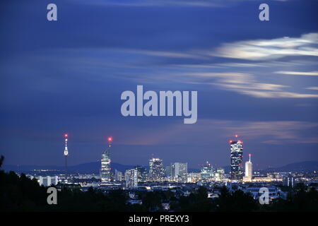 Modern cityscape skyline of Vienna Donaucity with skyscrapers with some illuminated windows and blurred clouds in the evening of a full moon night. Stock Photo
