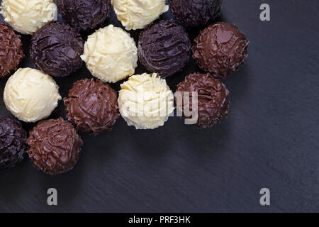 Delicious chocolate truffles on black stone background. Assortment of fine chocolates in white dark and milk chocolate. Stock Photo