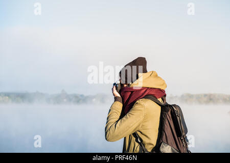 Female hiker photographing beautiful nature scenery covered in fog. Woman uses a vintage film camera standing in gorgeous nature park at dawn Stock Photo