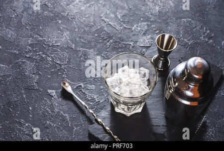 Bar tools for making cocktail. Shaker and a glass of ice on dark stone table. Copy space Stock Photo