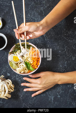 Female hands. Miso Ramen Asian noodles in bowls on dark stone background. Top view Stock Photo