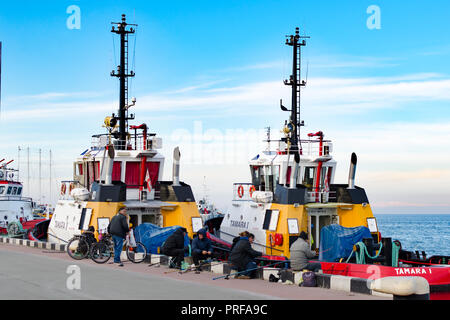 Batumi, Georgia, 2017-11-28: Embankment in the port with fishermen and moored ships. Stock Photo