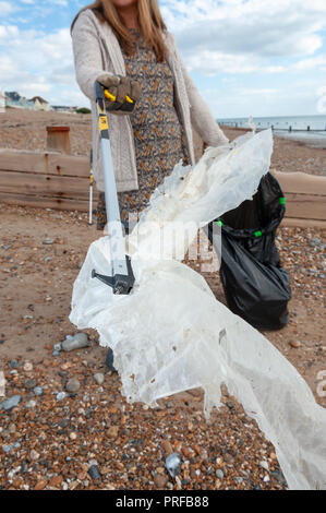 A woman picks up plastic waste using a litter picker from the beach during a community beach clean up. Stock Photo