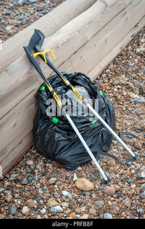 Beach clean up. A black bag full of rubbish collected from the beach and two litter pick up tools leaning on a wooden groyne on the beach. Stock Photo