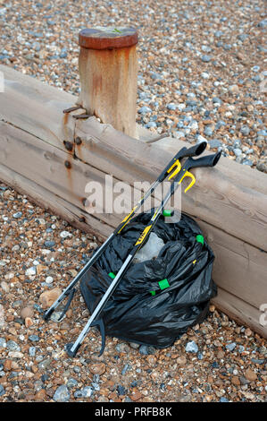 Beach clean up. A black bag full of rubbish collected from the beach and two litter pick up tools leaning on a wooden groyne on the beach. Stock Photo