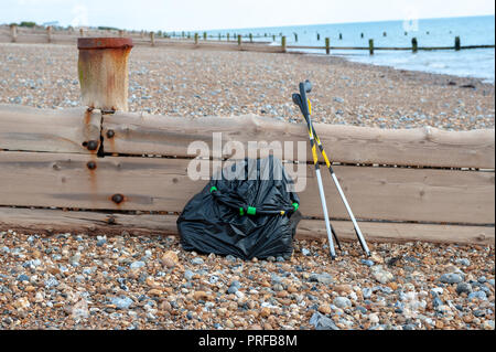 Beach clean up. A black bag full of rubbish collected from the beach and two litter pick up tools leaning on a wooden groyne on the beach. Stock Photo