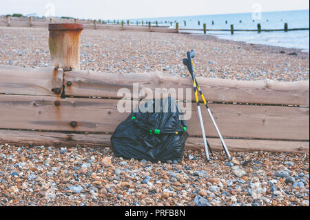 Beach clean up. A black bag full of rubbish collected from the beach and two litter pick up tools leaning on a wooden groyne on the beach. Stock Photo