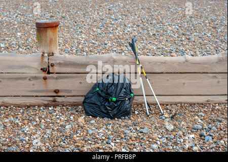 Beach clean up. A black bag full of rubbish collected from the beach and two litter pick up tools leaning on a wooden groyne on the beach. Stock Photo