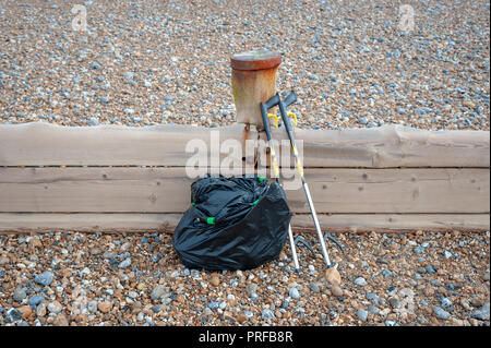 Beach clean up. A black bag full of rubbish collected from the beach and two litter pick up tools leaning on a wooden groyne on the beach. Stock Photo