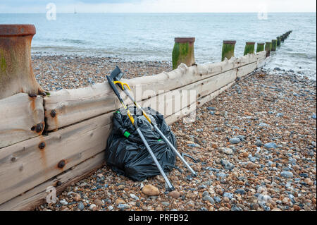 Beach clean up. A black bag full of rubbish collected from the beach and two litter pick up tools leaning on a wooden groyne on the beach. Stock Photo