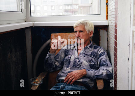 portrait of a gray-haired man 60 years old. A man sits in a chair and smokes a cigarette Stock Photo