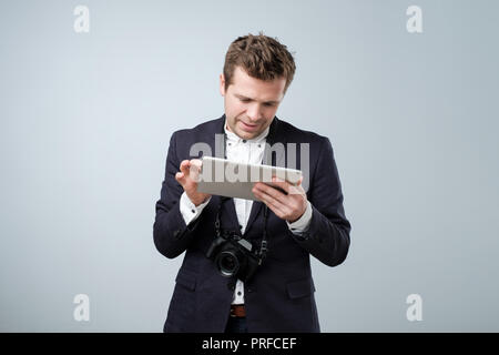 Portrait of a young man in suit using tablet computer over gray background and looking at screen Stock Photo