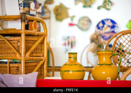 Decorative clay pots, bowls and vases standing on shelf in kitchen. Abstract paintings and colorful drawings on wall in the background. Bright sunligh Stock Photo