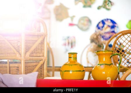 Decorative clay pots, bowls and vases standing on shelf in kitchen. Abstract paintings and colorful drawings on wall in the background. Bright sunligh Stock Photo