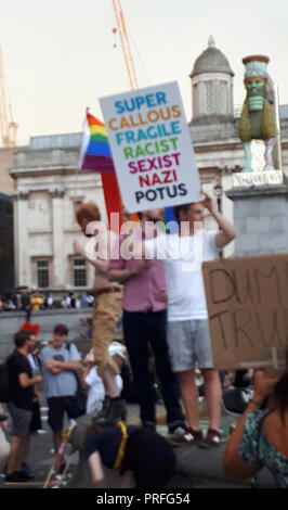 London UK, 13th July 2018. 100,000 people protest against the visit of the US President Donald Trump. The protesters gather in Trafalgar Square. A man holds a placard. A Gay Pride flag can be seen. Stock Photo