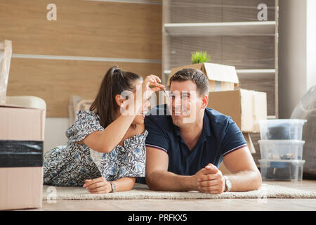 Happy new flat couple of owners showing keys sitting in the floor. Moving in day. Stock Photo