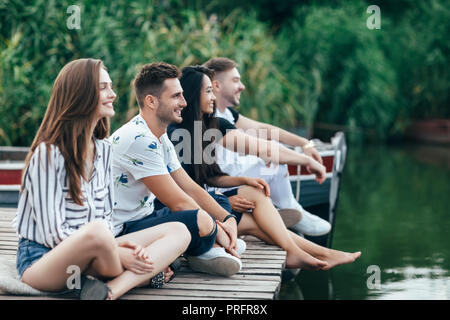 Group of happy young friends relaxing on river pier. Summer vacation concept Stock Photo