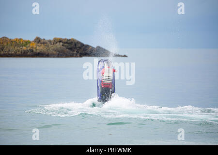 Rear view action shot of male jet skier having fun isolated out at sea, standing up on high speed jet ski bike, UK. Jet skiing, extreme watersports. Stock Photo