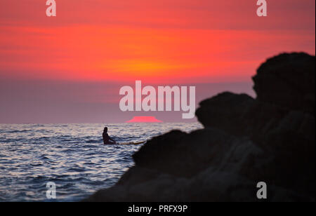 A surfer watching the sunset at Crackington Haven in Cornwall UK Stock Photo