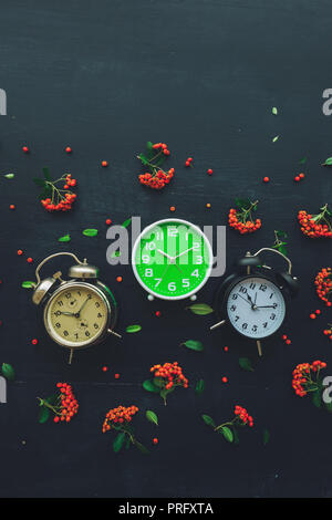 Ten past ten on three different alarm clock, flat lay top view minimal composition of timepieces placed on dark wooden background with decorative wild Stock Photo