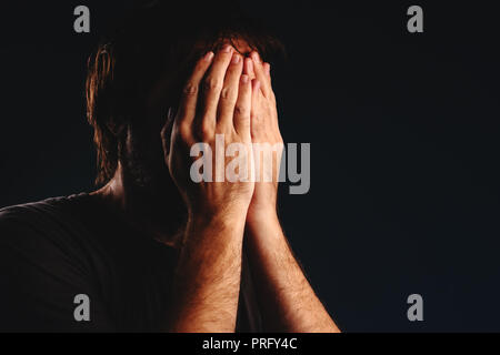Man is crying in despair, hands covering face, low key portrait Stock Photo