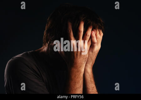 Man is crying in despair, hands covering face, low key portrait Stock Photo