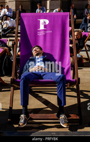 A Young Man Asleep In An Oversized Deck Chair During A Lunch Break, Paternoster Square, London, UK Stock Photo
