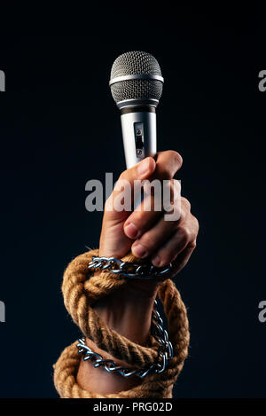 Freedom of the press and journalism, conceptual image with microphone in male hand tied with chains and ropes, low key image Stock Photo