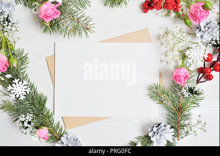 Mockup of Christmas Wreath in form of heart with sheet of paper Decorated with white snowflakes and cones. White wooden background with place for your Stock Photo