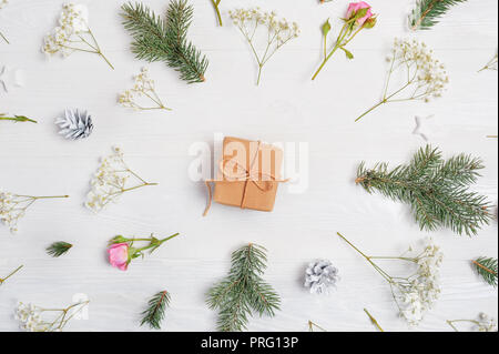 Abstract Christmas background decorated with gift in center and xmas elements - cones, tree branches, roses on a white wooden background. Stock Photo