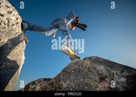 man stepping over boulders wearing walking shoes and carrying a camera. Stock Photo