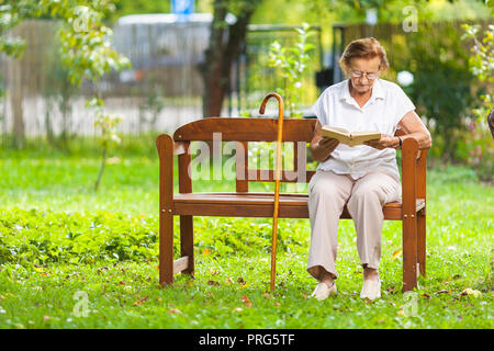 Elderly woman sitting and relaxing on a bench outdoors in park Stock Photo