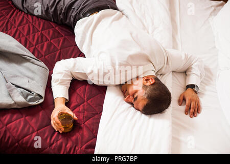 Businessman sleeping on a bed, holding glass of whiskey Stock Photo