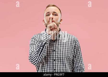 Secret, gossip concept. Young man whispering a secret behind his hand. Businessman isolated on trendy pink studio background. Human emotions, facial expression concept. Stock Photo